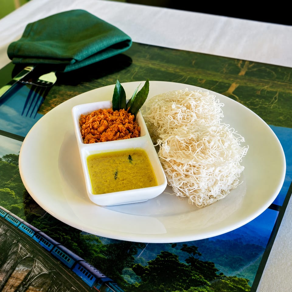 Plate of white rice noodles with yellow curry sauce and orange relish, garnished with fresh leaves on a restaurant table.