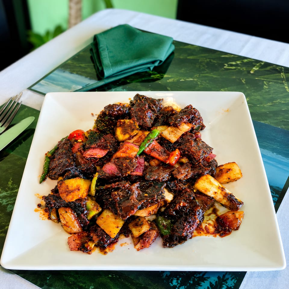 Glazed stir-fried beef with colorful peppers and vegetables served on a white square plate beside a folded teal napkin.