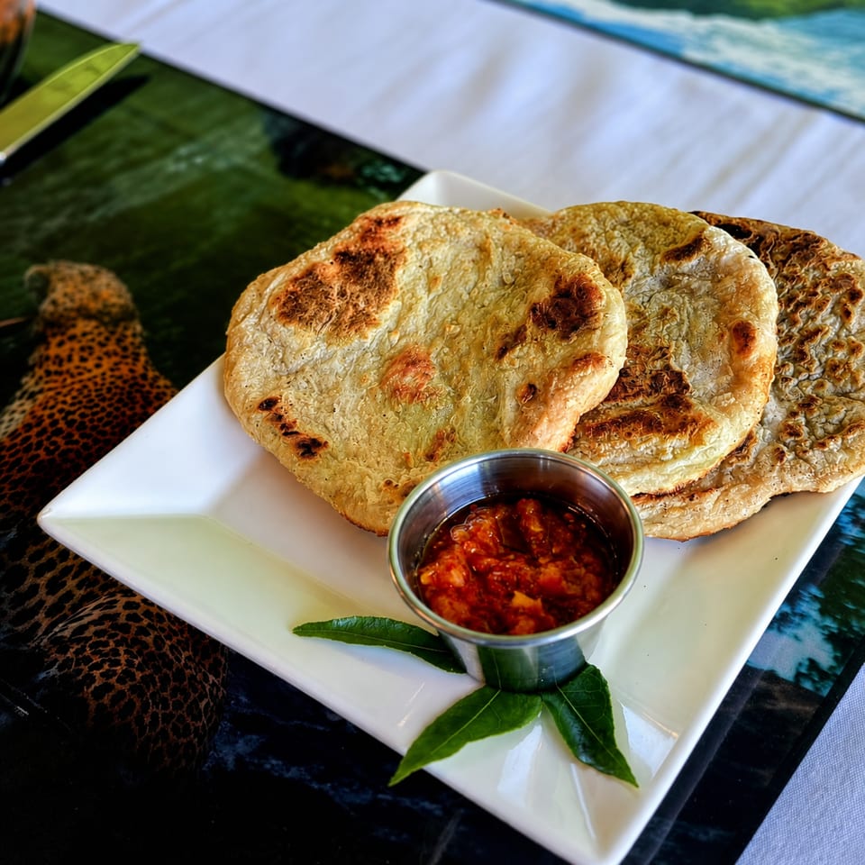 Grilled flatbreads served on a white plate with spicy red dipping sauce and fresh green leaves.